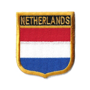 Könnte beinhalten: Ein gold gestickter Aufnäher mit dem Wort "NIEDERLANDE" in schwarzen Buchstaben auf schwarzem Hintergrund. Der Aufnäher zeigt die niederländische Flagge mit roten, weißen und blauen Streifen.