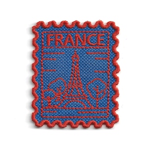 May include: A rectangular embroidered patch shaped like a postage stamp with a scalloped red border. The design features a blue fabric background with red thread stitching depicting the Eiffel Tower, two trees, and the word FRANCE at the top.