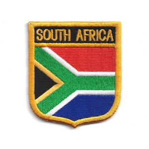 May include: Embroidered patch featuring the South African flag design. The patch has a shield shape with a gold border. The flag design includes red, green, blue, black, and white colors, with the text "SOUTH AFRICA" in black.
