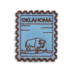 Peut inclure: Un écusson bleu clair avec une bordure marron festonnée. L'écusson comporte le mot "OKLAHOMA" en haut, avec une illustration de bison en dessous. Le design ressemble à un timbre-poste.
