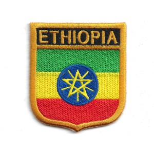 May include: Embroidered patch featuring the flag of Ethiopia. The patch has a shield shape with a gold border. The flag design includes green, yellow, and red stripes, a blue circle, and a yellow star in the center. The word "ETHIOPIA" is embroidered in gold.