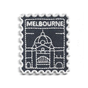 Può includere: Toppa ricamata blu navy a forma di francobollo. La toppa presenta un'illustrazione cucita in bianco di un edificio e la scritta "MELBOURNE" in alto. I bordi sono smerlati con filo bianco.