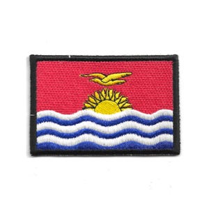 May include: Embroidered patch depicting the flag of Kiribati. The design features a red background, a yellow sun, a bird in flight, and blue and white waves. The patch is edged with a black border.