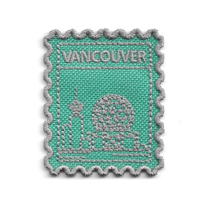 Peut inclure: Un écusson brodé rectangulaire en forme de timbre-poste avec un fond en tissu sarcelle et des coutures gris argenté. Le motif présente le mot VANCOUVER en haut et un contour stylisé de la ligne d'horizon de la ville incluant un dôme.