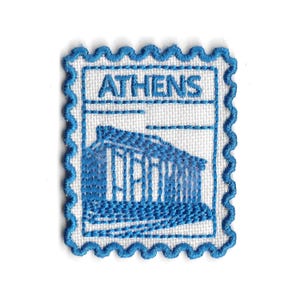 Pode incluir: Remendo bordado em forma de selo postal. O remendo apresenta uma ilustração azul de um templo grego e a palavra "ATHENS" em letras azuis sobre um fundo branco. A borda é um design azul ondulado.