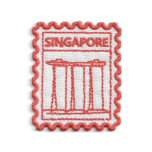 May include: A rectangular embroidered patch shaped like a postage stamp with a scalloped coral-colored border. The white fabric features the word SINGAPORE stitched in coral thread above a line drawing of the Marina Bay Sands hotel structure.