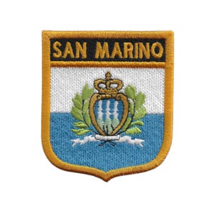 Puede incluir: Parche bordado con el escudo de armas de San Marino. El parche tiene un borde dorado y el texto "SAN MARINO" en letras doradas. El diseño presenta un escudo con una corona, ramas de laurel y una combinación de colores azul y blanco.