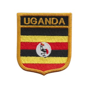 Könnte beinhalten: Gestickter Aufnäher mit dem Wort "UGANDA" über horizontalen Streifen in Schwarz, Gelb und Rot. Ein kreisförmiges Emblem mit einem Vogel ist mittig auf dem Aufnäher angebracht. Der Aufnäher hat einen goldenen Rand und eine Schildform.
