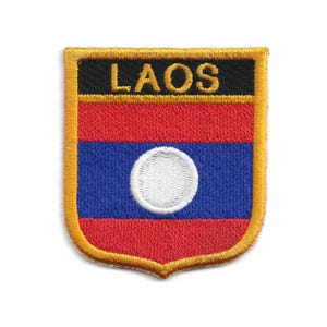 May include: Embroidered patch featuring the flag of Laos. The shield-shaped patch has a gold border and the word "LAOS" in gold letters on a black background. The flag design includes red and blue stripes with a white circle.