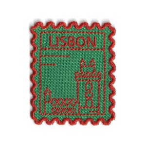 Puede incluir: Un parche bordado verde con un borde rojo festoneado. El parche presenta la palabra "LISBOA" en la parte superior y una ilustración estilizada de un edificio. La palabra "Portugal" está en la parte inferior. El diseño se asemeja a un sello postal.