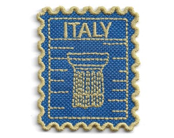 May include: A rectangular embroidered patch with a scalloped edge in tan thread. The patch features a blue background with the word ITALY stitched in tan at the top, above a tan embroidered graphic of a classical column with horizontal lines.