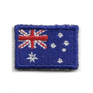 Puede incluir: Un parche rectangular con la bandera australiana. El diseño incluye la Union Jack en la esquina superior izquierda, una cruz roja de San Jorge, estrellas blancas y la constelación de la Cruz del Sur sobre un fondo azul.