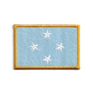 May include: Embroidered patch featuring the flag of the Federated States of Micronesia. The patch has a light blue background with four white stars and a gold border. The patch is rectangular in shape.