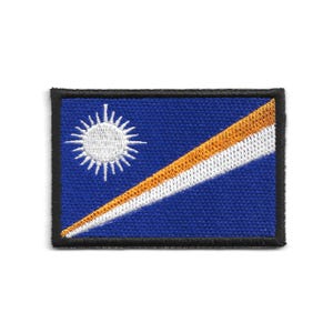 May include: Embroidered patch featuring the flag of the Marshall Islands. The design includes a blue background with a white sun in the upper left corner and a diagonal stripe of orange and white. The patch has a black border.