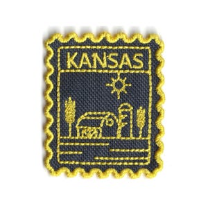 May include: Embroidered patch featuring a Kansas design. The patch has a dark blue background with yellow stitching. The word "KANSAS" is at the top, with a sun, farm, and trees. The patch has a yellow scalloped border.