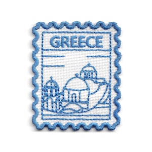 Può includere: Una toppa ricamata rettangolare con bordo smerlato, caratterizzata da uno sfondo bianco e filo blu. Il design raffigura un paesaggio stilizzato con edifici a cupola e la parola GREECE ricamata in blu nella parte superiore della toppa.