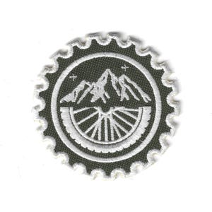 Op de afbeelding: Geborduurde patch met een berg- en fietswielontwerp. De patch heeft een donkergroene achtergrond met witte stiksels. De buitenrand heeft een geschulpte rand. Het ontwerp omvat een bergketen en een fietswiel.