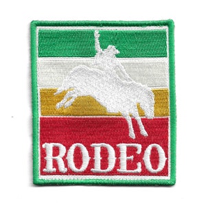 Op de afbeelding: Groen, wit, goud en rood geborduurd patch met een wit silhouet van een cowboy die een bokkend paard berijdt. Het woord "RODEO" is in wit onder het paard geborduurd.