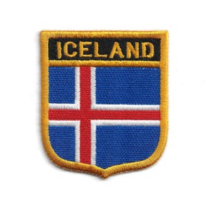 Può includere: Toppa ricamata con la bandiera islandese. Il design presenta uno sfondo blu con una croce rossa bordata di bianco. La parola "ICELAND" è ricamata in oro su uno stendardo nero nella parte superiore, con un bordo dorato.