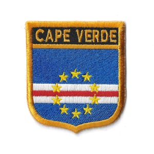 Op de afbeelding: Een geborduurde patch met de vlag van Kaapverdië. De patch heeft de vorm van een schild en heeft een gouden rand. De vlag is blauw met een witte streep en een rode streep. Er zijn tien gele sterren op de vlag.