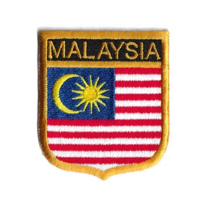 Könnte beinhalten: Ein gold gestickter Aufnäher mit dem Wort "MALAYSIA" in schwarzen Buchstaben und der malaysischen Flagge in der Mitte. Die Flagge zeigt einen gelben Halbmond und einen Stern auf blauem Hintergrund, mit 14 abwechselnden roten und weißen Streifen.