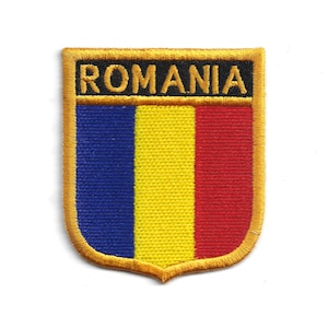 Puede incluir: Parche bordado con la bandera rumana. El parche tiene un borde dorado y forma de escudo. El diseño de la bandera incluye franjas verticales azules, amarillas y rojas, con la palabra "ROMANIA" en letras doradas sobre fondo negro.