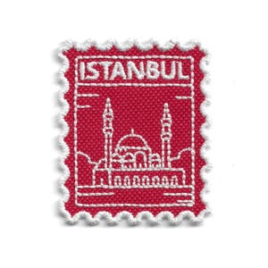 May include: A red fabric patch with white embroidered details. The patch is in the shape of a postage stamp with the word "ISTANBUL" at the top. The design features a mosque with minarets.