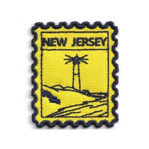 Könnte beinhalten: Gestickter Aufnäher in Form einer Briefmarke, mit gelbem Hintergrund und einer dunkelblauen Leuchtturmillustration sowie dem Text "NEW JERSEY". Der Aufnäher hat einen dunkelblauen, gewellten Rand.
