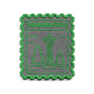 May include: Embroidered patch featuring a gray background with a green outline and details. The design includes the text "WASHINGTON", the Space Needle, and evergreen trees. The patch has a decorative, scalloped edge.