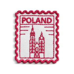 Può includere: Una toppa ricamata rettangolare con bordo smerlato in filo rosa brillante su base in tessuto bianco. Il design presenta la parola POLAND in lettere rosa in grassetto sopra un disegno stilizzato a linee di una chiesa a due torri.