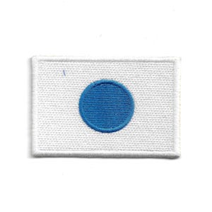 May include: Embroidered patch featuring the flag of Japan. The patch is rectangular with a white background and a centered blue circle. The edges are finished with a white border.
