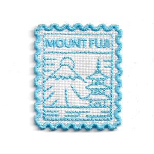 Può includere: Toppa ricamata con un disegno azzurro del Monte Fuji e di una pagoda, con la scritta "MOUNT FUJI". La toppa ha uno sfondo bianco e un bordo smerlato azzurro.