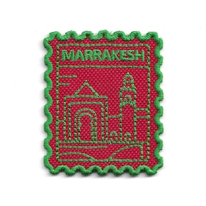 May include: Embroidered patch featuring a red background with a green border and stitching. The patch depicts a stylized illustration of buildings and the word "MARRAKESH" in green.