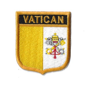 Può includere: Una toppa ricamata gialla e bianca con la parola "VATICAN" in lettere nere su uno sfondo dorato. La toppa presenta uno stemma con una chiave e una tiara papale.