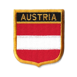 Op de afbeelding: Een rood, wit en gouden geborduurde patch met het woord "AUSTRIA" in zwarte letters. De patch heeft de vorm van een schild.