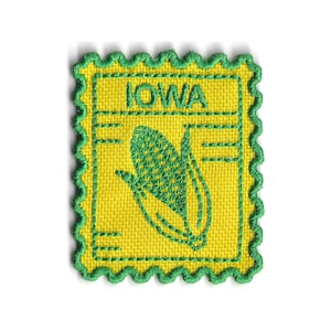 May include: Embroidered patch with a yellow background and a green border. The patch features the word "IOWA" and a green corn graphic. The square patch has a scalloped edge, reminiscent of a postage stamp.