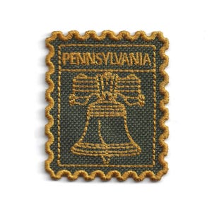 Puede incluir: Parche bordado con la Campana de la Libertad, con la palabra "PENNSYLVANIA" en la parte superior. El parche tiene un fondo verde oscuro con costuras doradas. Los bordes son festoneados.