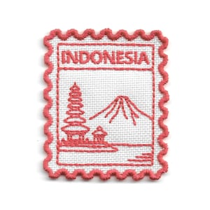 Può includere: Una toppa ricamata rettangolare con bordo smerlato in filo rosa corallo su base in tessuto bianco. Il design presenta la parola INDONESIA in lettere maiuscole sopra un'illustrazione cucita di una pagoda a più piani e una cima di montagna.
