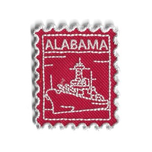 Peut inclure: Un écusson en tissu rouge avec un motif brodé blanc d'un navire et le mot "ALABAMA". L'écusson a un bord festonné et est probablement un souvenir ou un objet de collection.