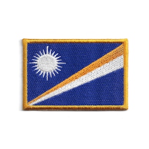 May include: Embroidered patch featuring the flag of the Marshall Islands. The design includes a blue background, a white sun in the upper left corner, and a diagonal stripe with white and orange sections. The patch has a gold border.