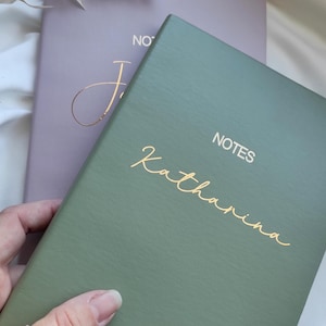 Könnte beinhalten: Ein grünes Notizbuch mit den Worten "NOTES" und "Katharina" in goldener Schrift.