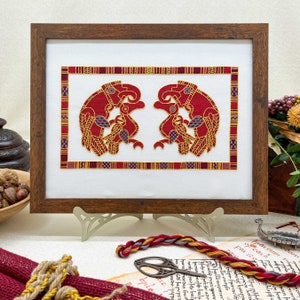 May include: Framed embroidery of two red stylized birds facing each other, with gold accents and a red, white, and gold patterned border.