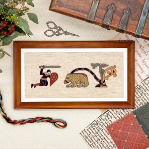 May include: A framed cross-stitch embroidery depicting a knight kneeling with a sword and shield, a bear, and a stylized tree. The embroidery is on a beige linen fabric and is framed in a dark wood frame.