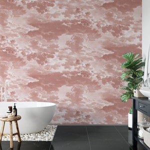 May include: A white bathtub sits in a bathroom with a pink and white cloud patterned wallpaper. The bathroom has a black tiled floor and a black side table with a plant on top.