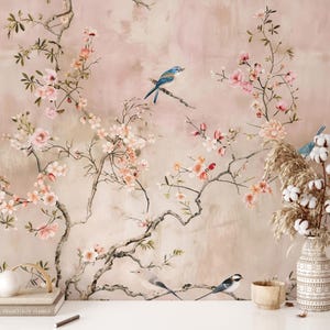 May include: A mural featuring a soft pink and beige background with blossoming branches and birds. The branches are adorned with pink flowers and green leaves. Several birds are perched on the branches. A vase with cotton and dried plants is on a white surface.