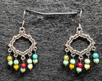 May include: A pair of silver-toned earrings with a decorative openwork design. Each earring features a diamond-shaped frame with dangling colorful beads in yellow, red, turquoise, and cream colors. The earrings have a hook closure.