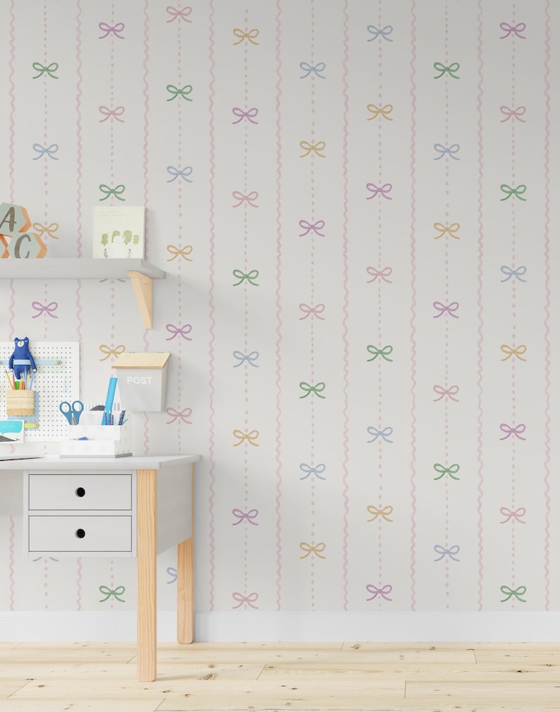 May include: A white wall decorated with a repeating pattern of pastel bows and wavy lines. The bows are in pink, green, yellow, and blue. A desk with a pegboard, shelf, and a small mailbox is in the foreground.