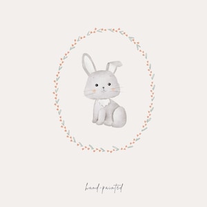 May include: A watercolor illustration of a gray bunny sitting inside a wreath of green leaves and pink flowers. The text "hand-painted" is written below the wreath.