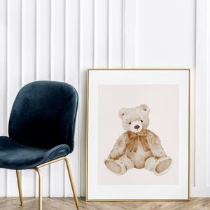 May include: A watercolor painting of a brown teddy bear sitting with a brown bow. The bear is sitting on a light beige background. The painting is framed in a gold frame.