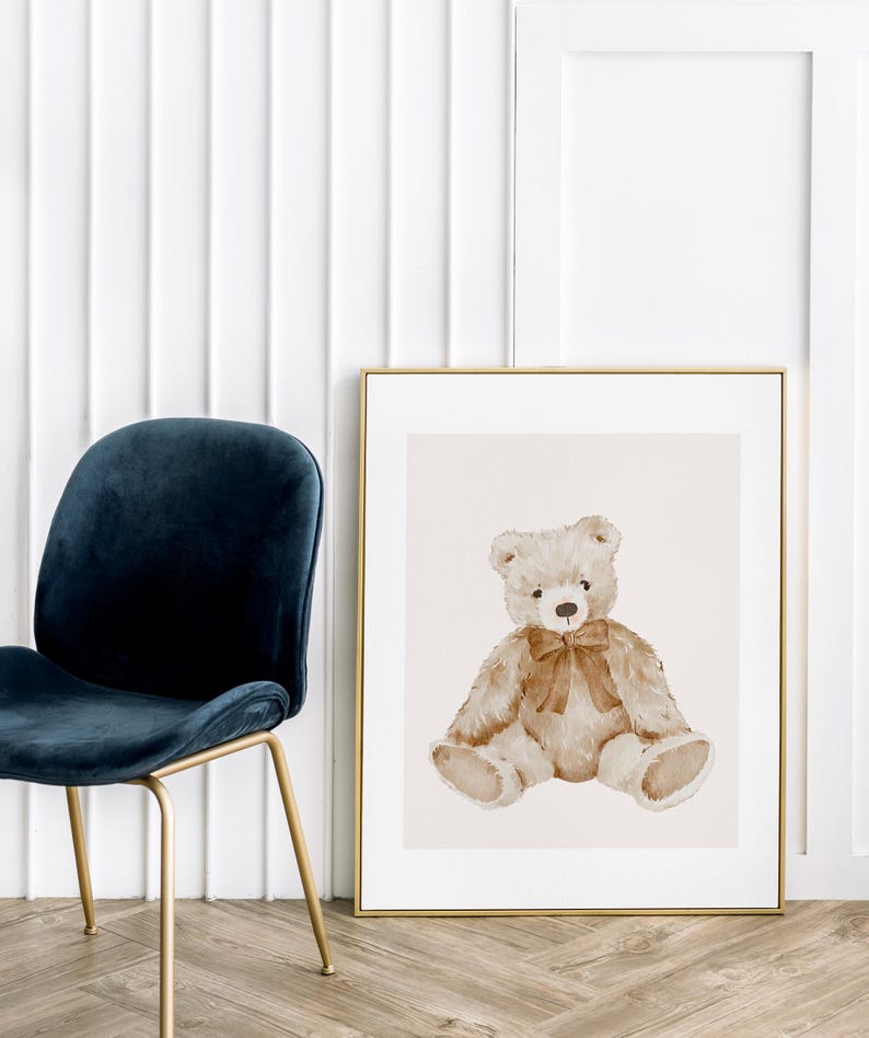 May include: A watercolor painting of a brown teddy bear sitting with a brown bow. The bear is sitting on a light beige background. The painting is framed in a gold frame.